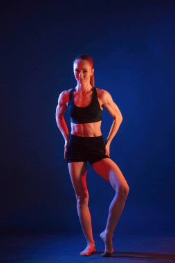 Duruyorum, poz veriyorum. Güzel kaslı kadın stüdyoda neon ışıklı..