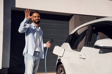 Merhaba, jest. Şarj kablosu duruyor. Genç şık adam, gündüz vakti elektrikli arabayla geziyor..