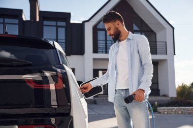 Aracı şarj etme işlemi. Genç şık adam, gündüz vakti elektrikli arabayla geziyor..