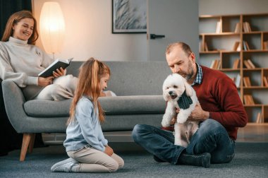 Adam malta köpeğiyle oynuyor. Anne ve kızı izliyor..