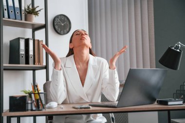 Oturuyor, gülümsüyor ve el kaldırıyor. Resmi giyinmiş güzel bir kadın ofiste çalışıyor..