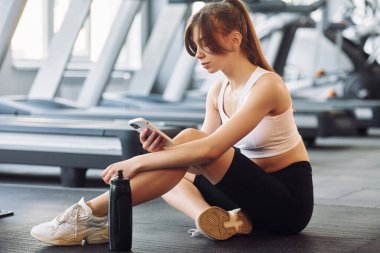 Akıllı telefon sizin ellerinizde. Spor elbiseli genç bir kadın spor salonunda spor yapıyor..