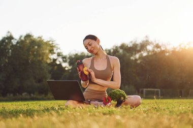 Laptop ve sebzelerle oturmak. Yoga elbiseli genç bayan dışarıda, sahada..