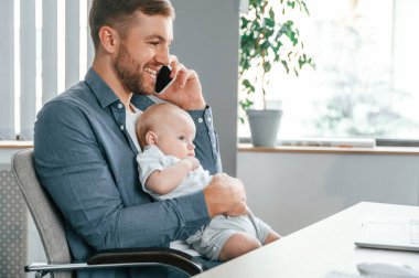 Telefonla konuşuyorum. Yürüyen bebekle baba içeride, ofiste..