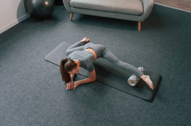 Paspasın üzerinde köpüklü rulo ile. Yoga elbiseli genç bir kadın içeride spor yapıyor..