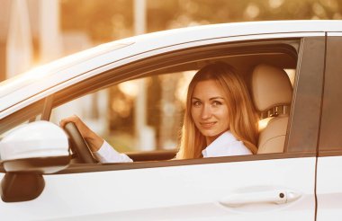 Otururken araba kullanmak. Beyaz elbiseli genç bir kadın gündüz vakti elektrikli arabasıyla geliyor..