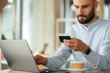 Kredi kartıyla ödeme yapmak. Genç adam kafede oturuyor ve bilgisayarını kullanarak çalışıyor..