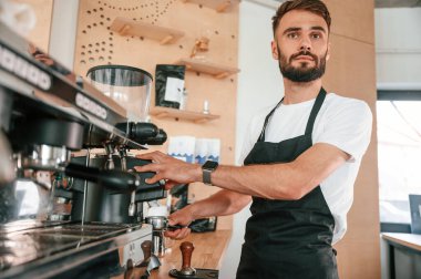 Kahve makinesini hazırlıyorum. Beyaz gömlekli ve siyah önlüklü kafe çalışanı içeride..