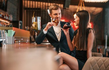 Yan görüş. Kadın ve erkek barda oturmuş içki içiyorlar..