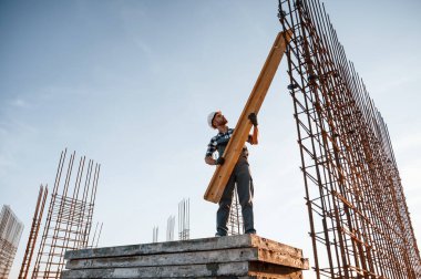 Gri üniformalı. Tahta tutuyorlar. Gündüz vakti inşaatta çalışan bir adam var..