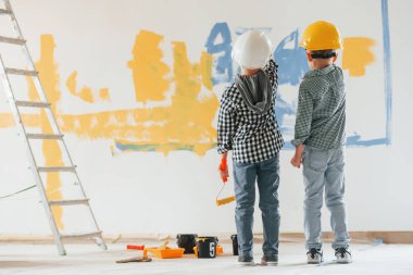 Sert şapkalarla. İki çocuk ev odasında duvar boyuyor..