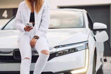 Akıllı telefonlu. Beyaz elbiseli genç bir kadın gündüz vakti elektrikli arabasıyla geliyor..