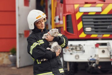 Büyük bir kamyona karşı durup güzel bir kediyi tutmak. Üniformalı kadın itfaiyeci departmanda çalışıyor..