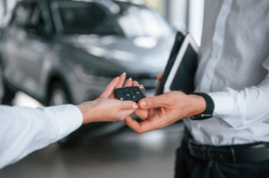 Yeni otomobilin anahtarları. Manzarayı kapat. Beyaz elbiseli bir adam araba galerisinde birlikte..