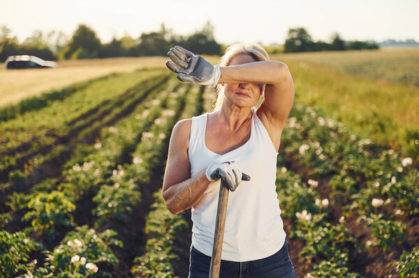 Tired of work. With showel. Woman is on the agricultural field at daytime.