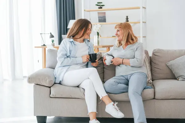 stock image Talking with each other. With cups of drink in hands. Mother and daughter is together at home.