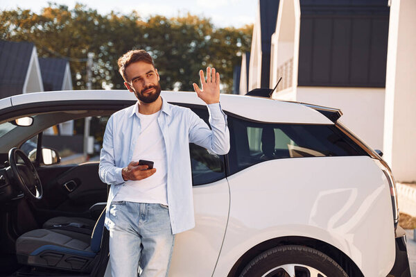 Привет, жест. Молодой стильный мужчина с электромобилем в дневное время.