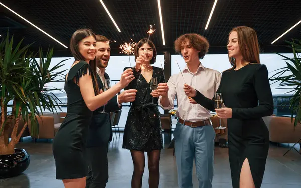 stock image Amazing sparklers. Group of people in beautiful elegant clothes are celebrating New Year indoors together.