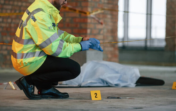 В перчатках. Мужчина-детектив собирает улики на месте преступления рядом с трупом на стройке.