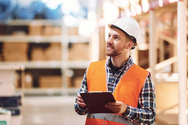 Using notepad. Employee in uniform is working in the storage at daytime.