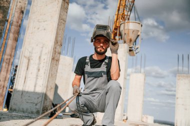 Kaynak maskesiyle. Üniformalı adam inşaat alanında çalışıyor..