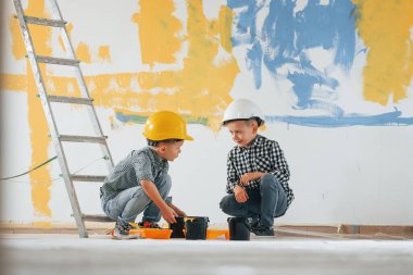 Mavi ve sarı arka plan. İki çocuk ev odasında duvar boyuyor..