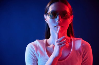 Sessizlik jesti. İçerideki neon ışıkta duran genç bir kadının portresi..