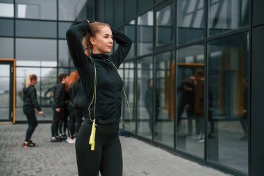 Atlama halatıyla ayakta duruyor. Bir grup sportif kadın dışarıda, siyah binanın yakınında..