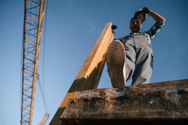 Aşağıdan bak. Büyük tahta parçasıyla. Gündüz vakti inşaatta çalışan bir adam var..