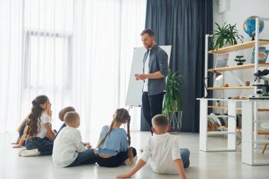 Ayakta durup beyaz tahta kullanarak dersi açıklamak. Okulda öğretmenle birlikte bir grup çocuk öğrenci..