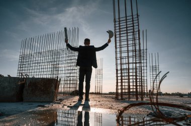 Ellerini kaldır. Akşam vakti ayakta. İnşaat alanında resmi kıyafetli bir işadamı var..