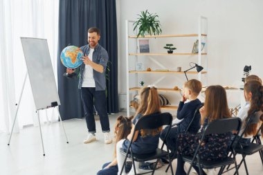 Dünya küresini kullanarak coğrafya dersi veriyorum. Okulda öğretmenle birlikte bir grup çocuk öğrenci..