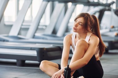 Yerde dinleniyor. Spor elbiseli genç bir kadın spor salonunda spor yapıyor..