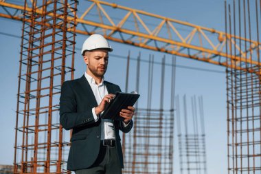 Kağıdı plan ve tabletle tutarak. Resmi kıyafetli bir işadamı gün içinde şantiyede olacak..