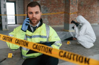 Adam telefonla konuşuyor. Dedektifler cesedin yanındaki suç mahallinde kanıt topluyorlar..