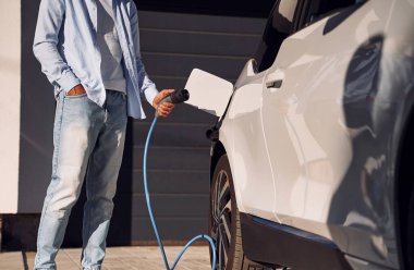 Kabloyu şarj ediyorum. Genç şık adam, gündüz vakti elektrikli arabayla geziyor..