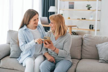 Akıllı telefon kullanıyor. Anne ve kızı evde birlikteler..