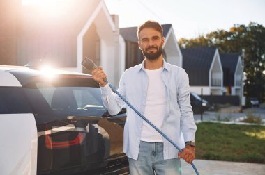 Güzel güneş ışığına karşı. Şarj kabloları duruyor. Genç şık adam, gündüz vakti elektrikli arabayla geziyor..