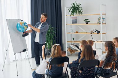 Coğrafya dersi. Ellerinde küreyle. Okulda öğretmenle birlikte bir grup çocuk öğrenci..