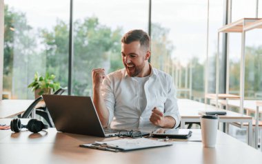 Başarılı bir proje. Kutlama ve mutluluk kavramı. Resmi kıyafetli adam modern ofiste çalışıyor..