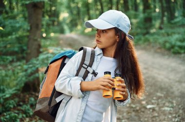Sarı renkli dürbünle. Kız yaz günü ormanda yeni yerler keşfediyor..