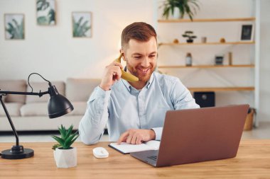 Telefonun başında konuşuyormuş gibi yapıyorsun. Masanın başında dizüstü bilgisayarı olan bir adam oturuyor ve eğleniyor..