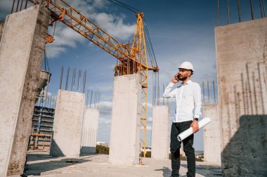 Telefonla konuşmak ve belgeleri elinde tutmak. Üniformalı adam inşaat alanında çalışıyor..