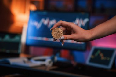 Bitcoin 'i bilgisayar ekranına ve tablete karşı grafiklerle tutan kadının elini kapat.
