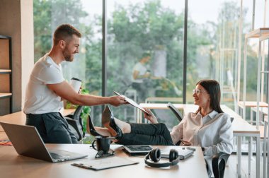 Sakin ol, bacaklar masanın üstünde. Erkek ve kadın modern ofiste birlikte çalışıyorlar..