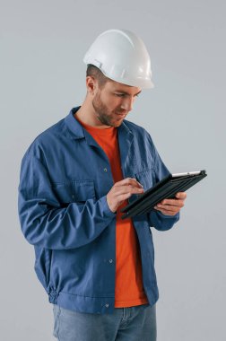 Başlıklı inşaat işçisi tabletle birlikte. Yakışıklı adam stüdyoda beyaz arka plana karşı..