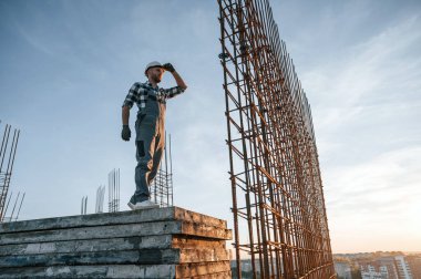 Büyük metal nesnelerin yanında. Gündüz vakti inşaatta çalışan bir adam var..