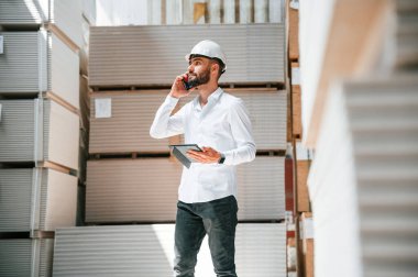 Resmi kıyafetler içinde ciddi bir yönetici. Depo işçisi depoda bir sürü ürünle birlikte..