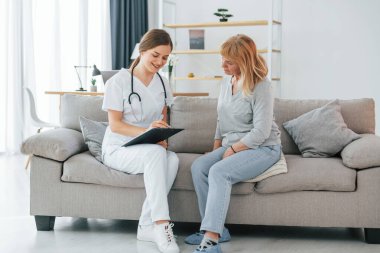 Hemşire reçete yazıyor. Üst düzey bir kadın, içeride genç bir bayan doktorla görüşüyor..