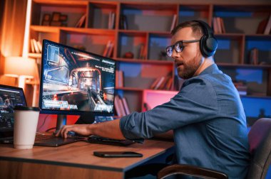 Konsantre adam bilgisayarında nişancı oyunu oynuyor. Neon ışıkları.